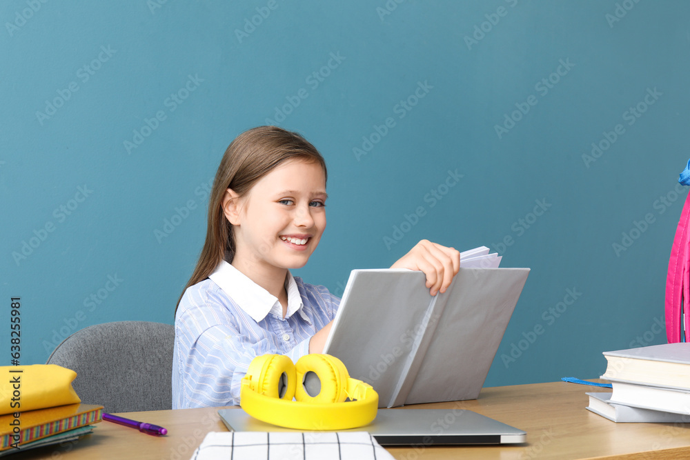 Little girl reading schoolbook at table on blue background