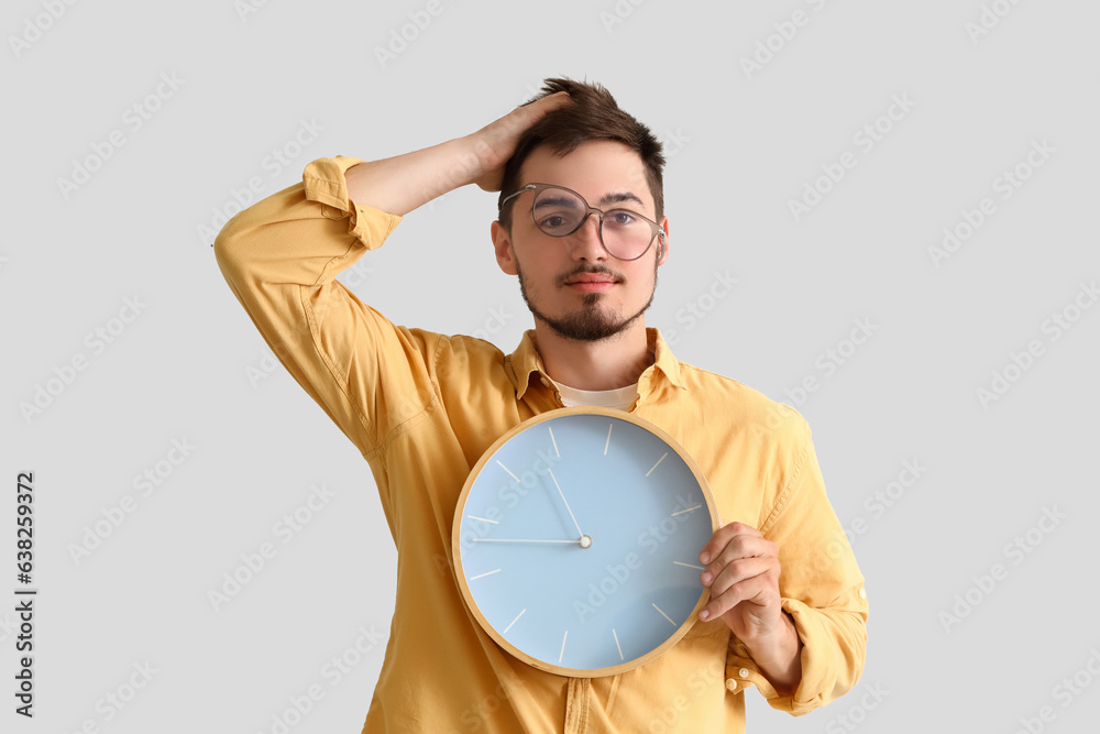 Stressed young man with clock on light background. Deadline concept