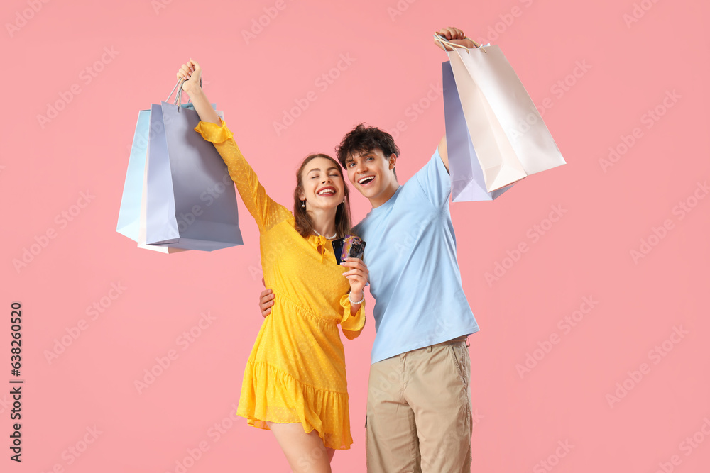 Happy young couple with shopping bags on pink background