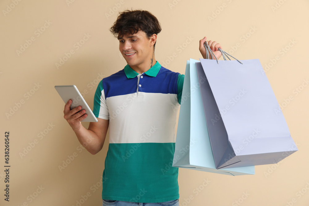 Young man with shopping bags on beige background