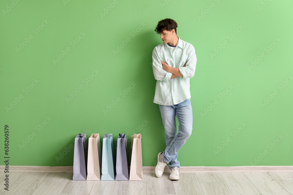 Young man with shopping bags near green wall