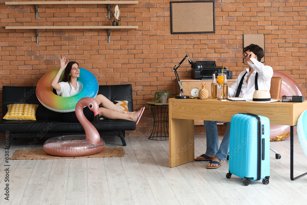 Young couple with beach accessories ready for summer vacation in office