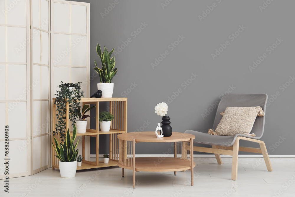 Light wooden coffee table with shelving unit and armchair near grey wall