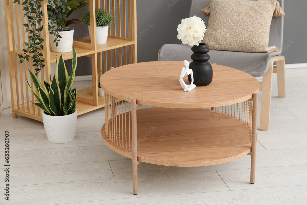 Light wooden coffee table with shelving unit and armchair near grey wall