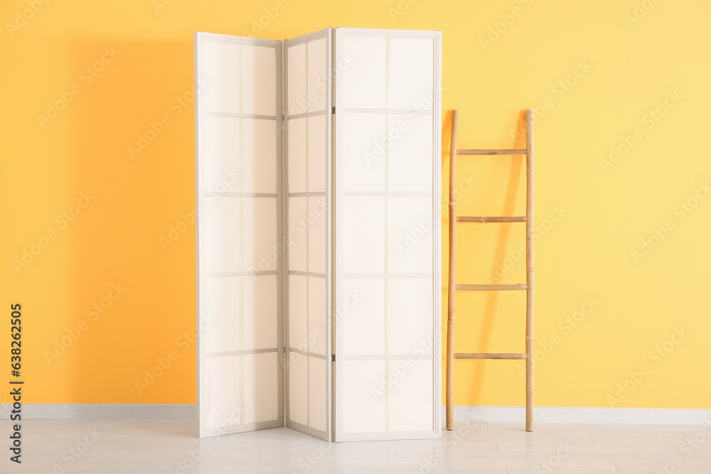 Folding screen and ladder near orange wall