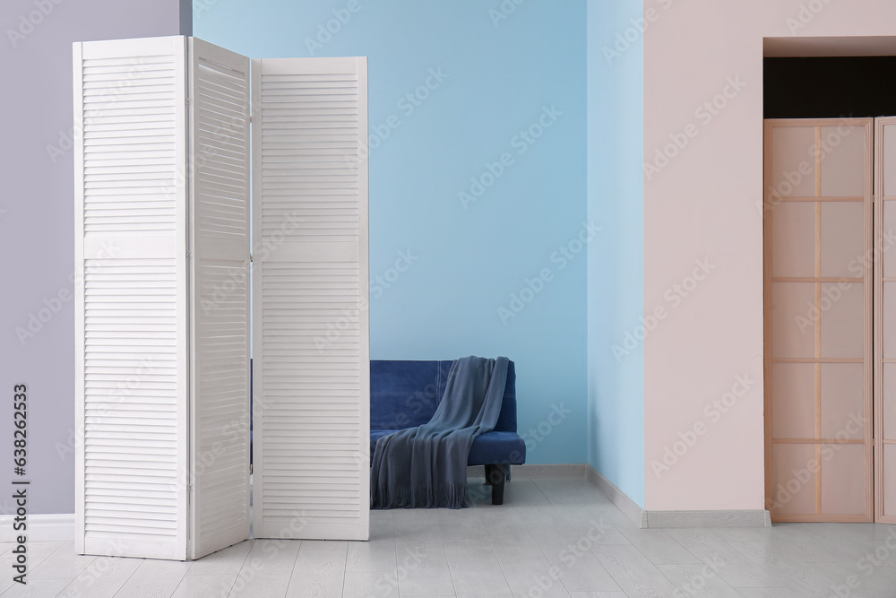 Folding screen, sofa and blanket near colorful wall