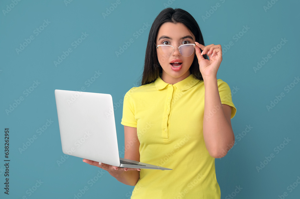 Shocked young female programmer with laptop on blue background