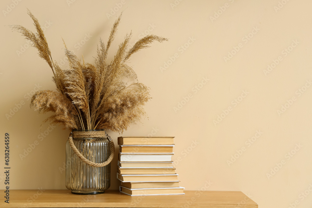 Stack of books and vase with pampas grass on shelf near beige wall