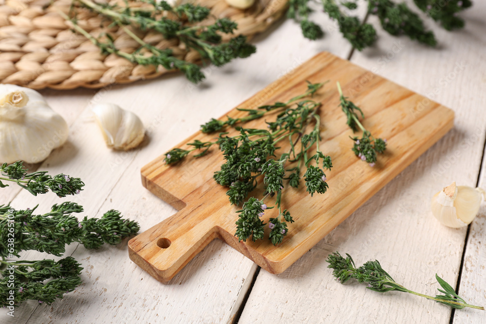 Cutting board with fresh thyme and garlic on light wooden background