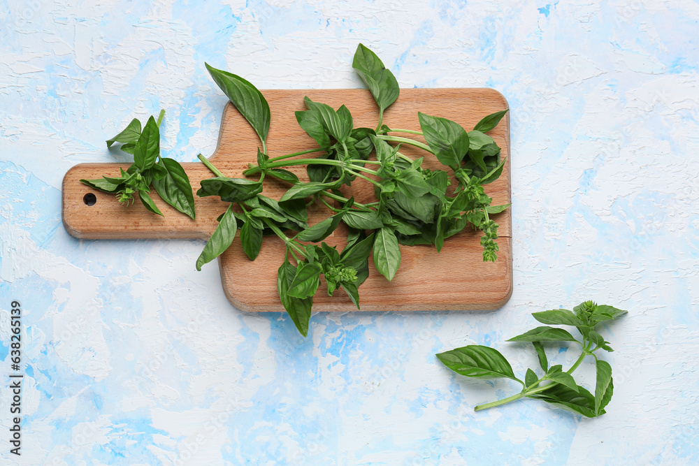 Wooden board with fresh basil on color background