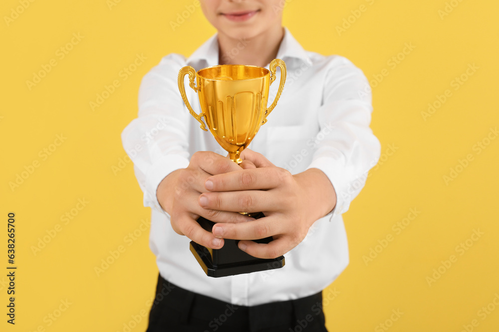 Smart little school boy with prize cup on yellow background, closeup