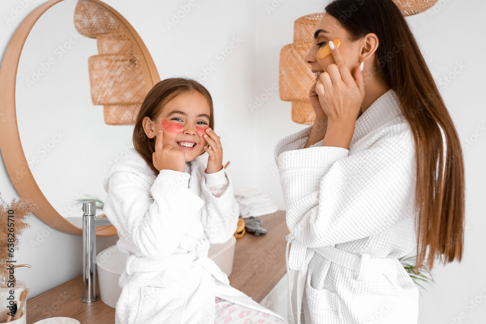 Happy mother and her little daughter with under-eye patches in bathroom