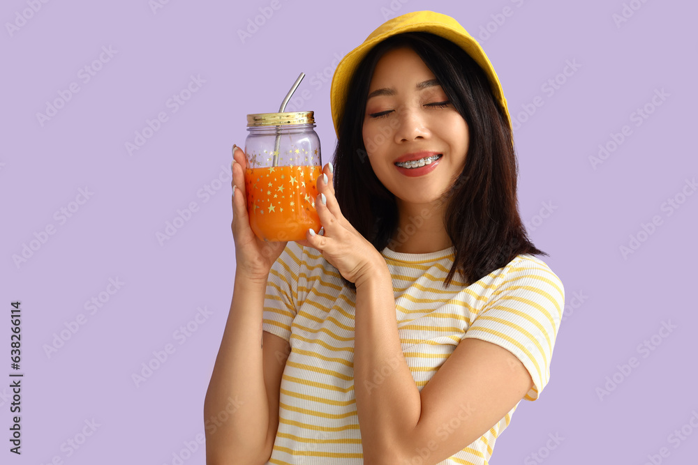 Beautiful Asian woman with glass jar of juice on lilac background