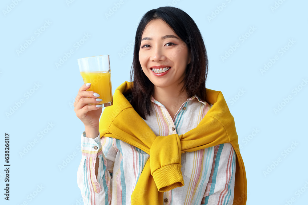 Beautiful Asian woman with glass of juice on blue background