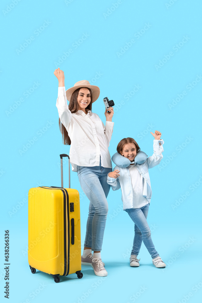 Happy mother with her little daughter and suitcase on blue background