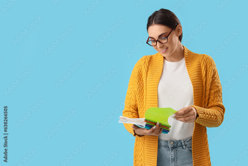 Young female teacher with copybooks on light blue background