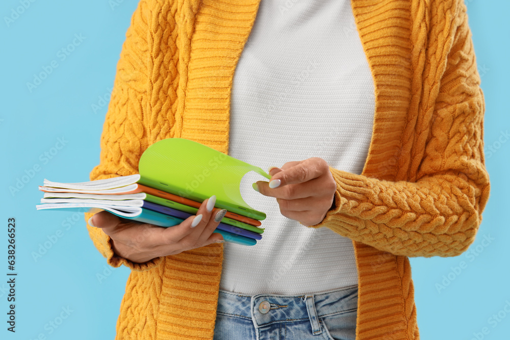 Young female teacher with copybooks on light blue background, closeup