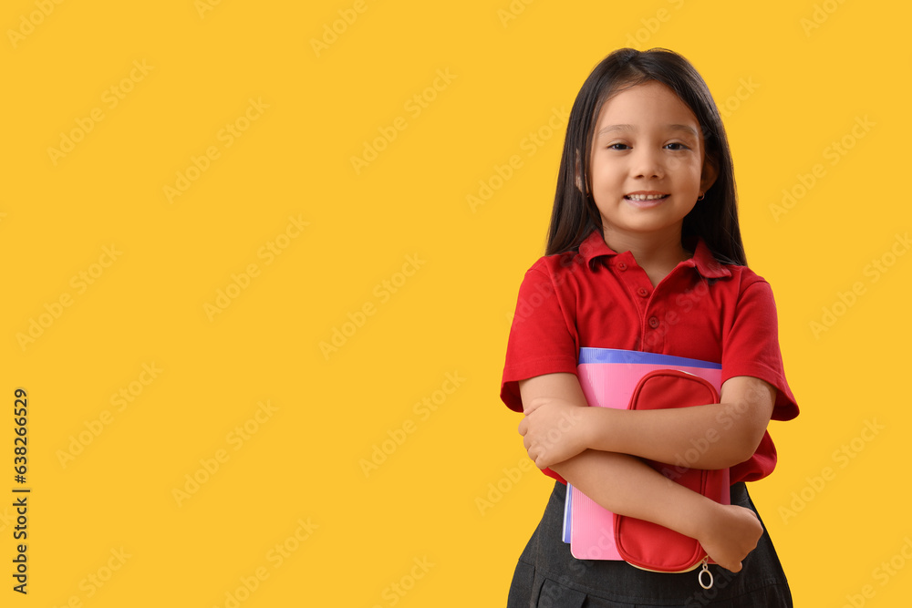 Little school girl with stationery on yellow background