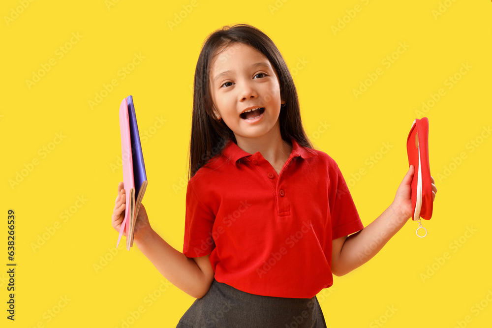 Little school girl with stationery on yellow background