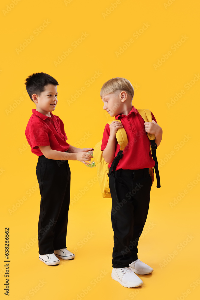 Little school boys with backpack on yellow background