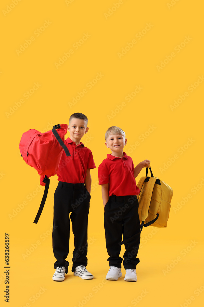 Little school boys with backpacks on yellow background