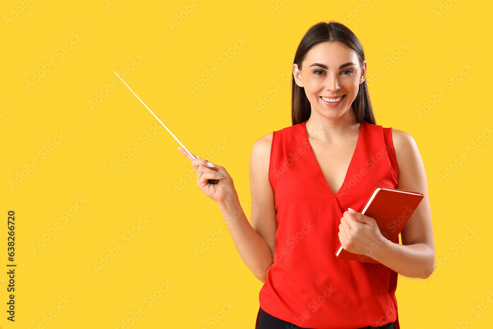 Young female teacher with pointer and notebook on yellow background