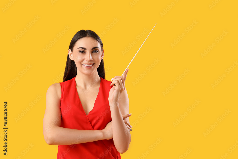 Young female teacher with pointer on yellow background