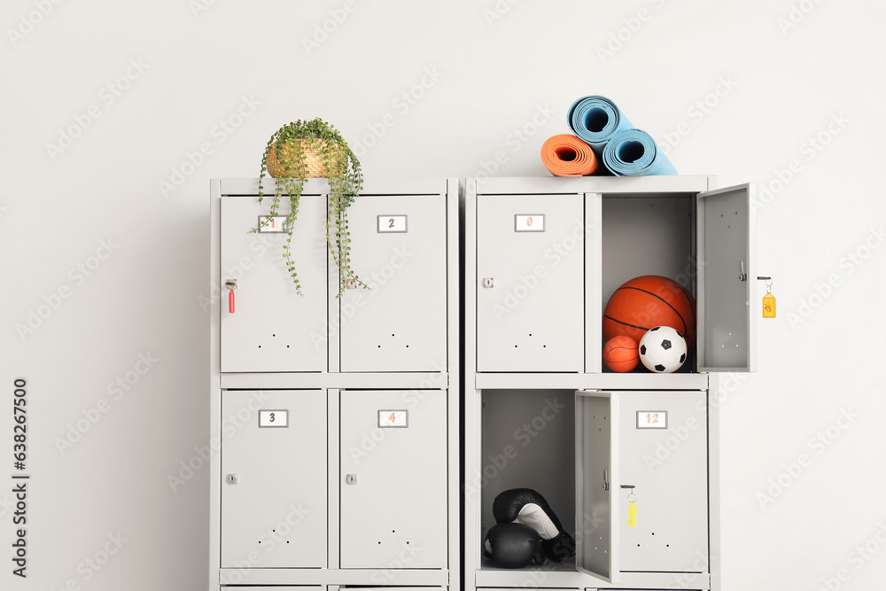 Modern locker with sports equipment and plant near light wall