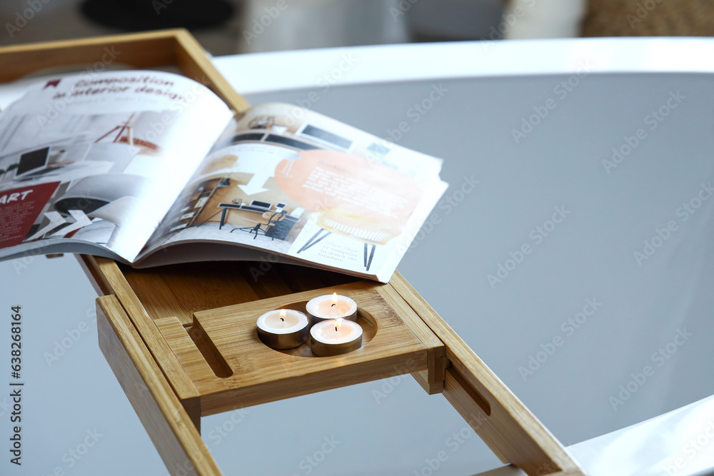 Wooden bathtub tray with burning candles and magazine in bathroom, closeup