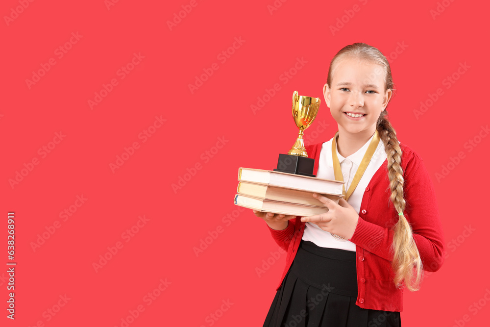 Cute little schoolgirl with gold cup and books on red background