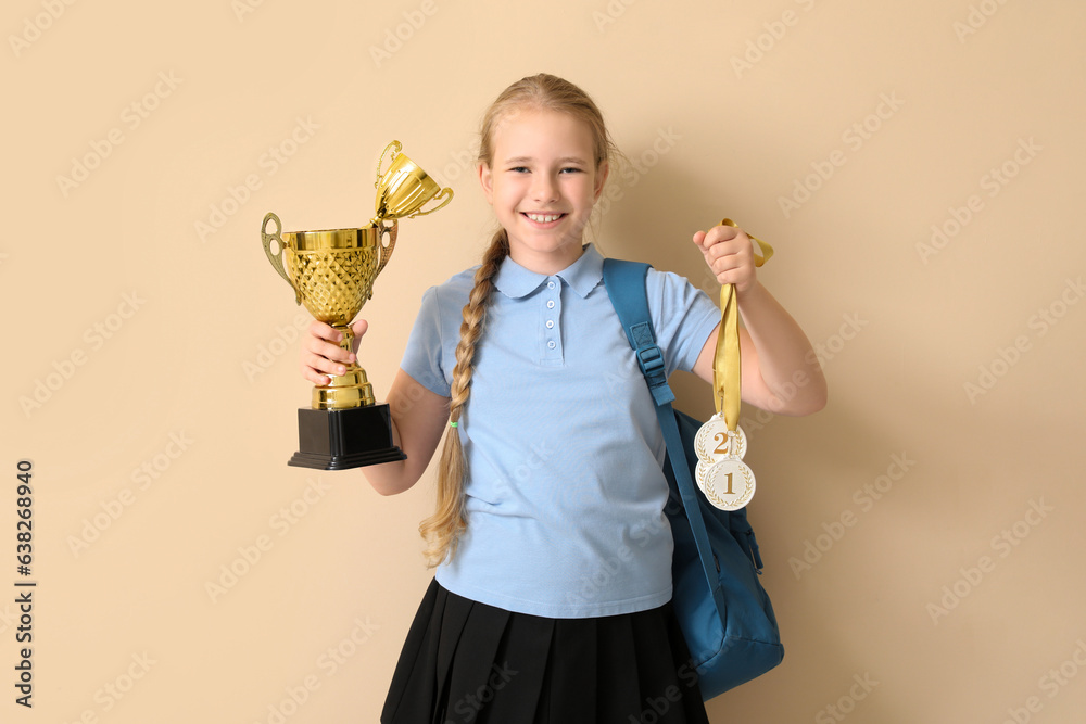 Cute little schoolgirl with gold cups and medals on beige background