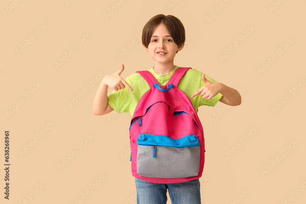 Little boy pointing at backpack on beige background