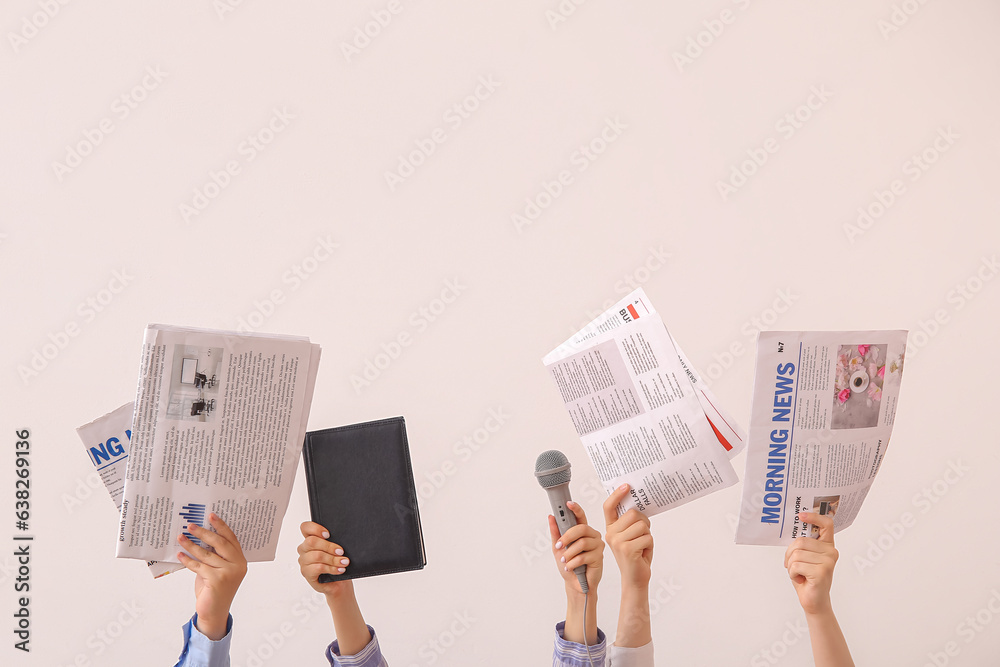 Female hands with different newspapers, notebook and microphone on light background