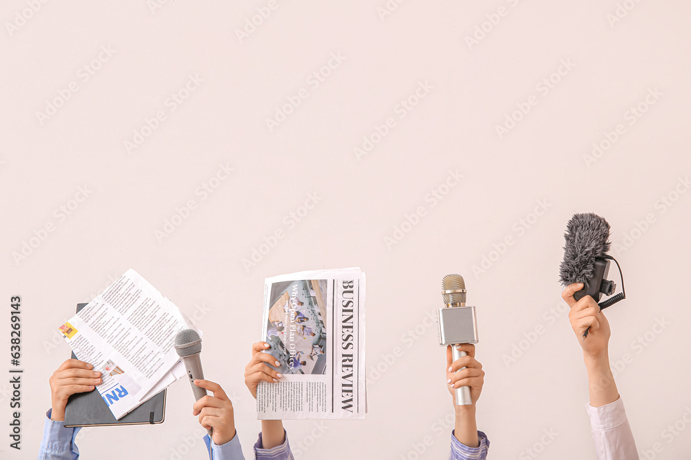 Female hands with newspapers and microphones on light background