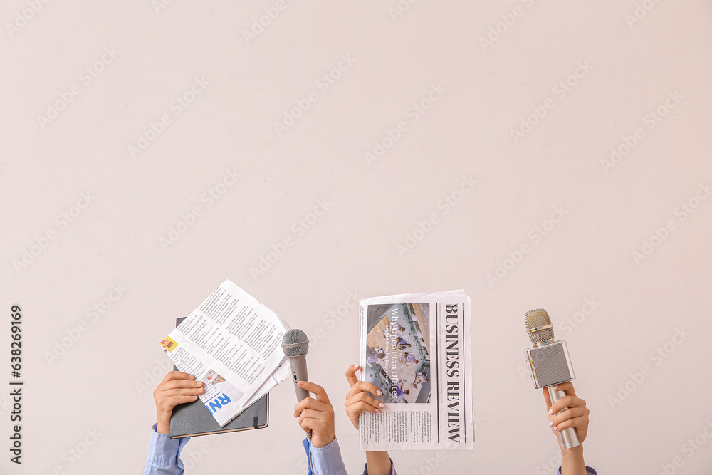 Female hands with newspapers and microphones on light background