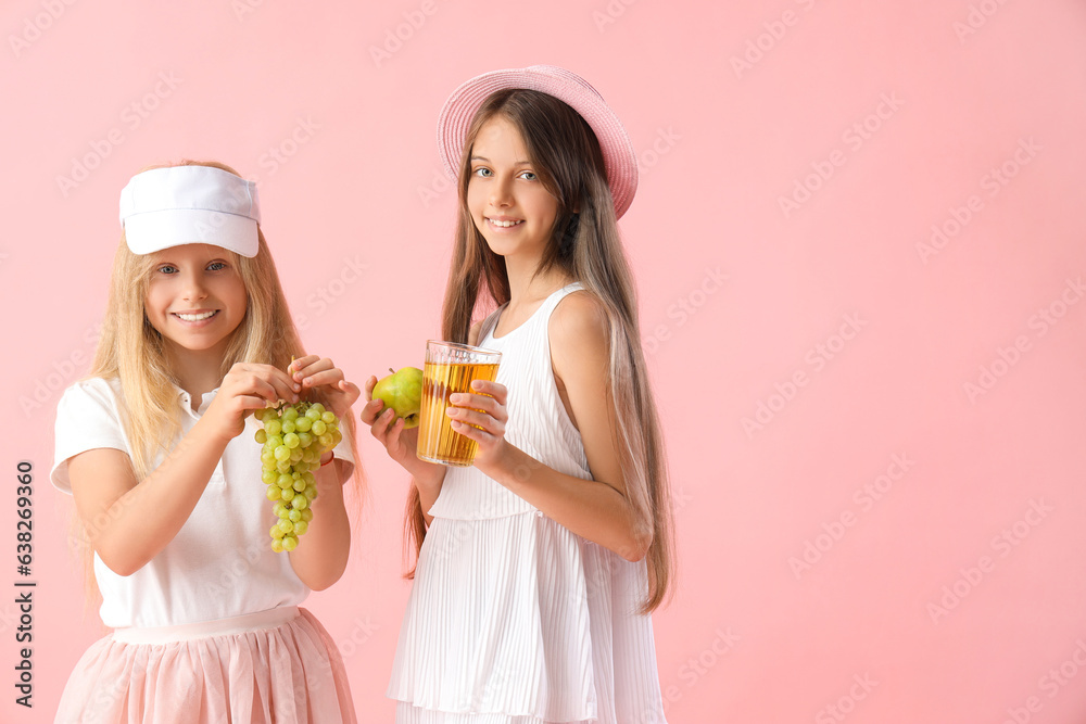 Little girls with glass of juice, grapes and apple on pink background