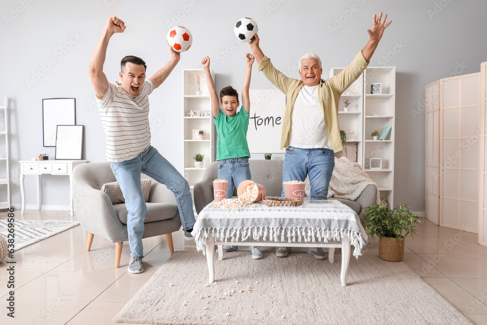 Happy little boy with his dad and grandfather watching football game at home