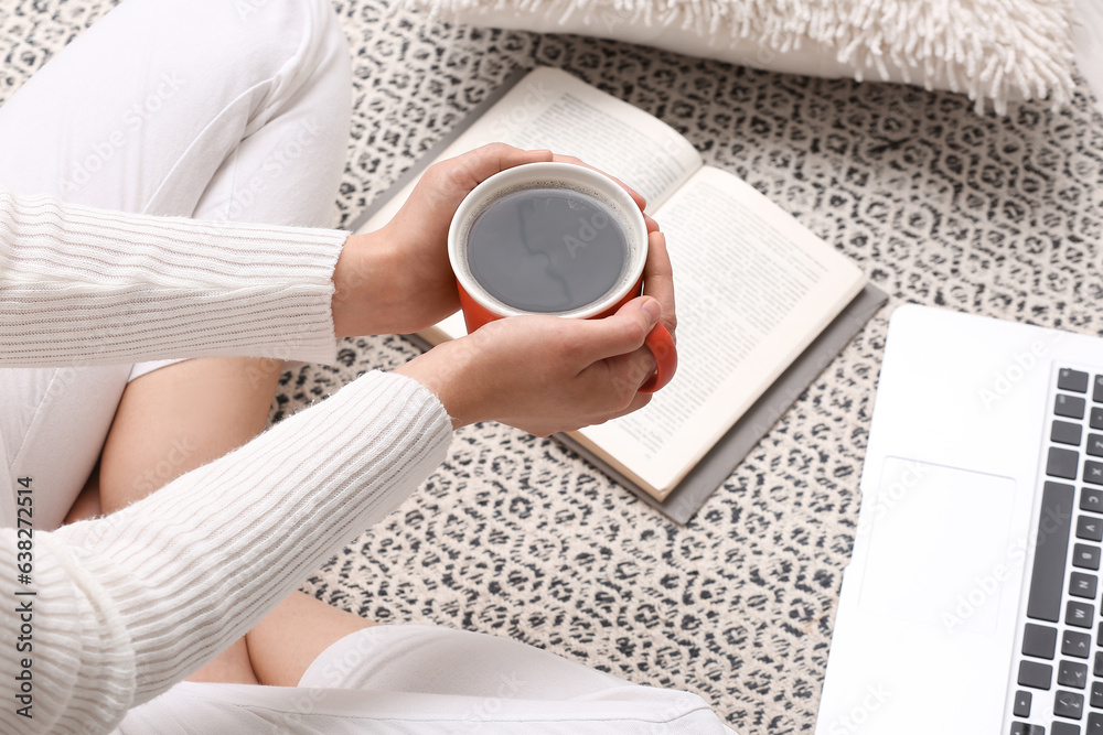 Woman with cup of coffee and book sitting on floor at home