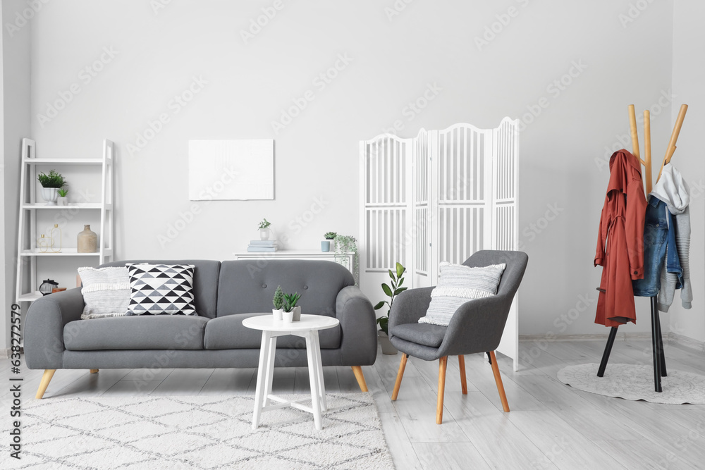 Interior of light living room with cozy armchair and grey sofa