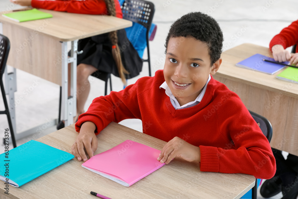 Little African-American schoolboy sitting at desk during lesson in classroom