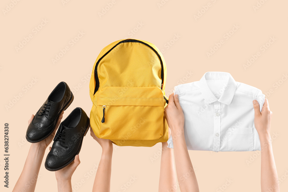 Female hands holding backpack and school uniform on beige background