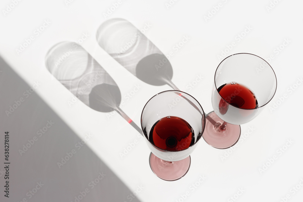 Minimal summer scene with glass of red wine, sunlight shadow on white background, copyspace, winegla