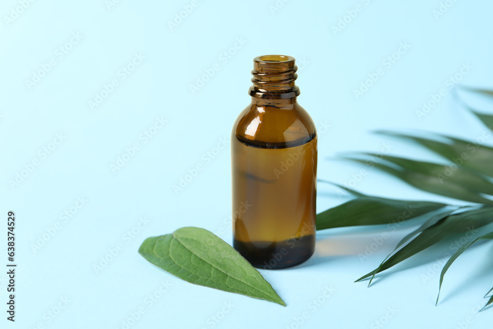 Bottle of cosmetic oil and leaves on light blue background, closeup