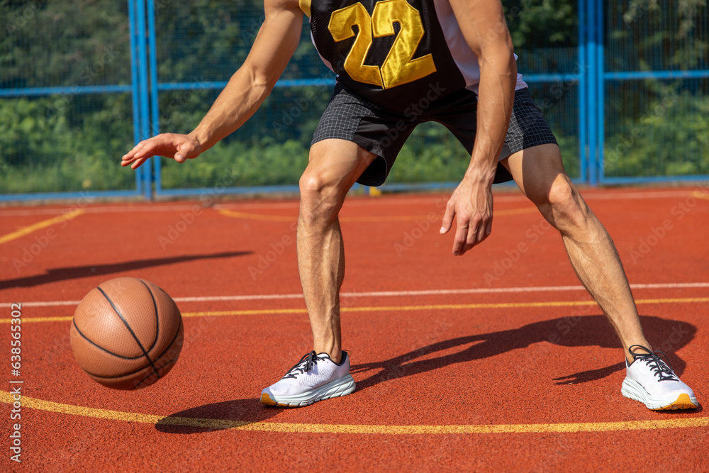 Muscular legs of unrecognizable basketball player training in outdoor court.