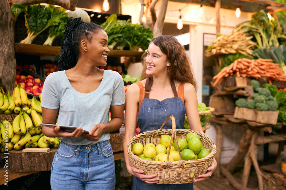 Two Women With Basket Of Lemons And Digital Tablet Working At Fruit And Vegetable Stall In Market