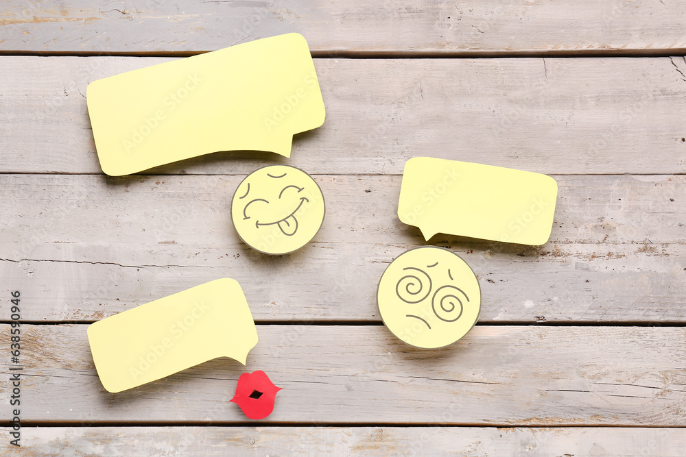 Paper faces and lips with blank speech bubbles on grey wooden background