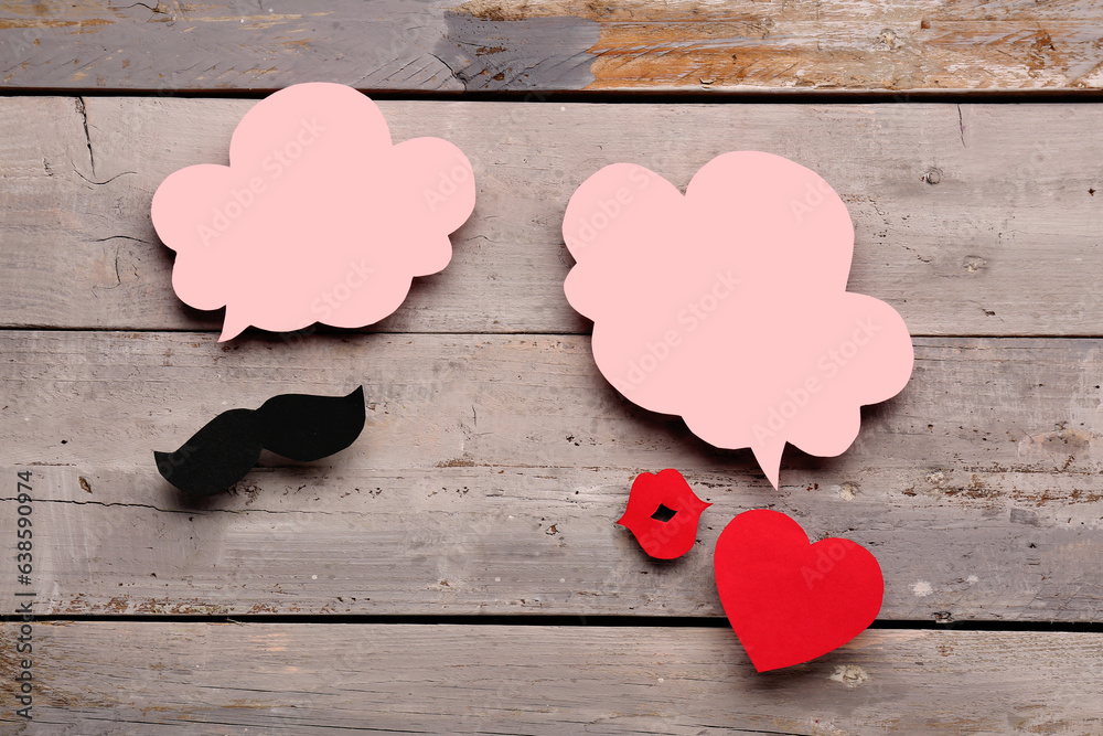 Paper mustache, lips and heart with blank speech bubbles on grey wooden background