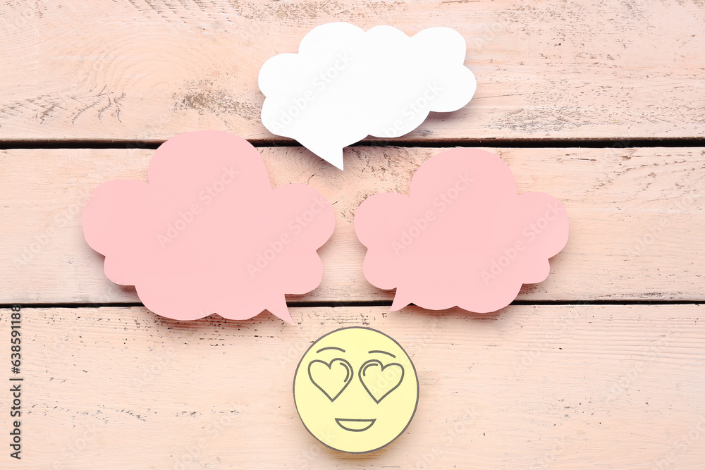 Paper face with heart eyes and blank speech bubbles on beige wooden background