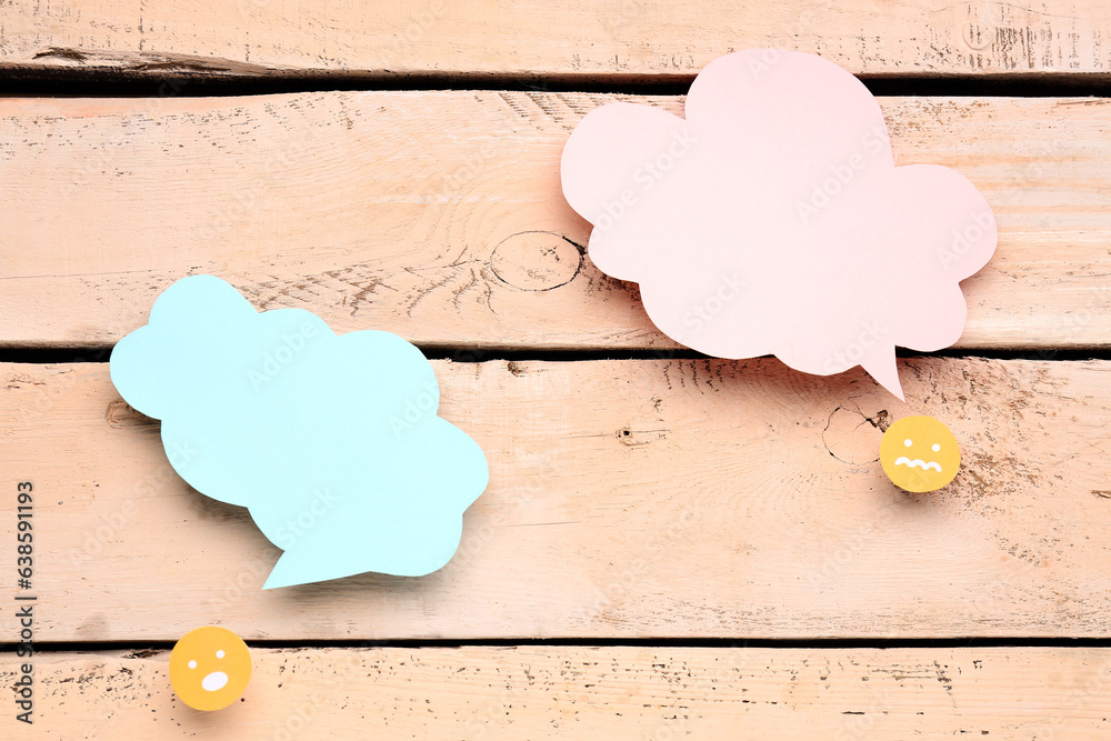 Paper faces with blank speech bubbles on beige wooden background