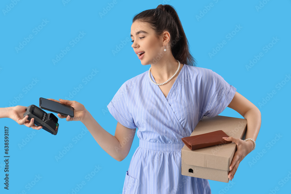 Young woman paying for shoes with credit card on blue background